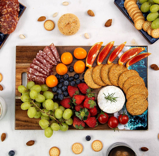 Wooden charcuterie board with fruits, meats, and cheeses on a white surface.